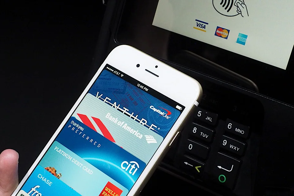 iPhone displaying payment cards beside a contactless checkout terminal