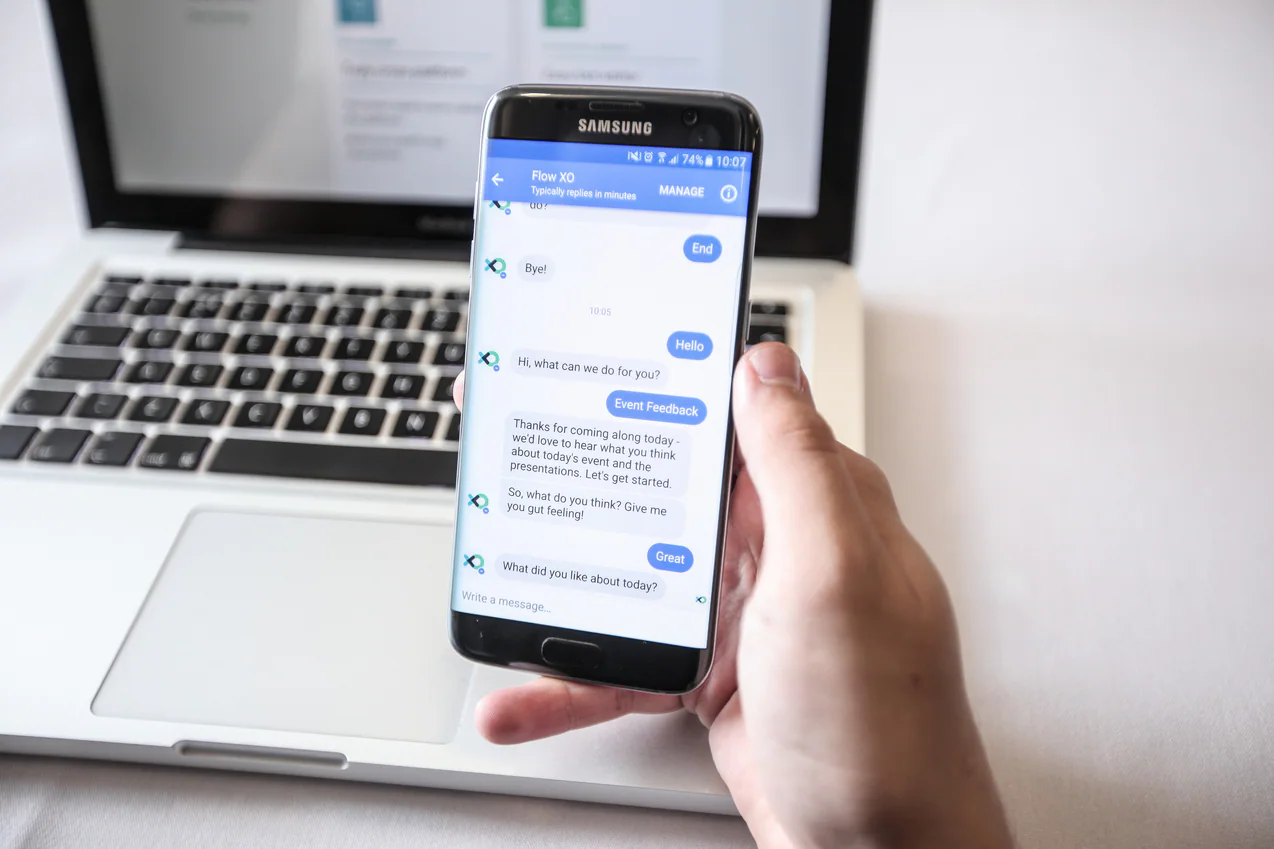 Person using a chatbot on a smartphone beside a laptop
