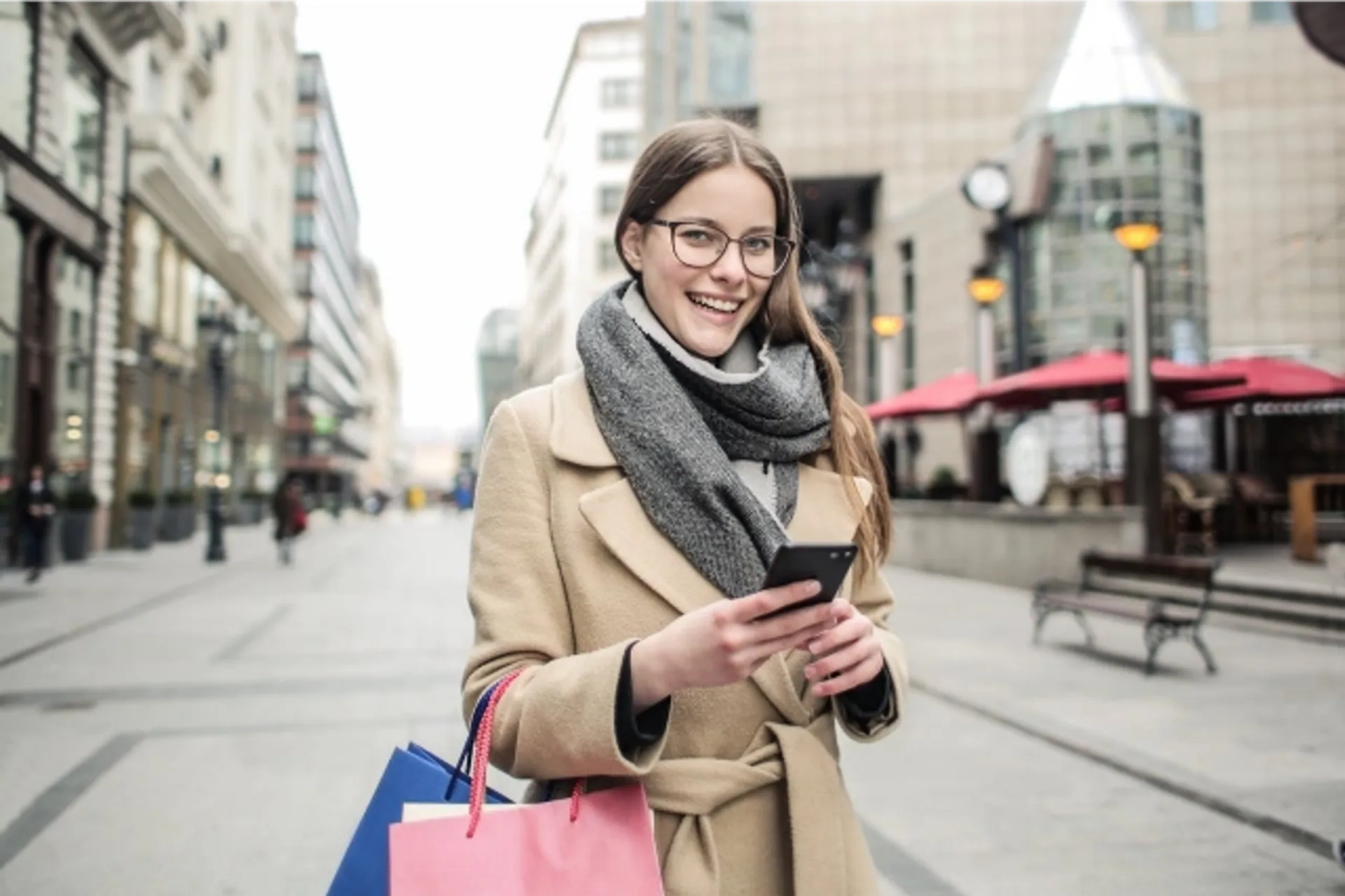 Shopper holding a smartphone and shopping bags on a city street