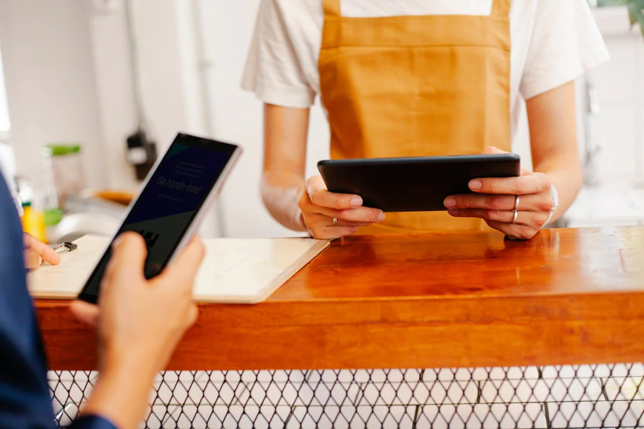 Customer showing a smartphone at a checkout counter while a cashier holds a tablet
