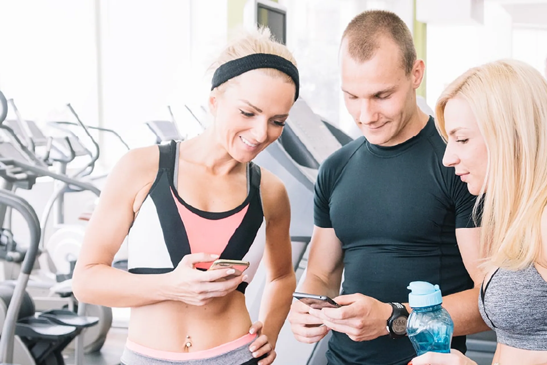 Three people looking at phones in a gym