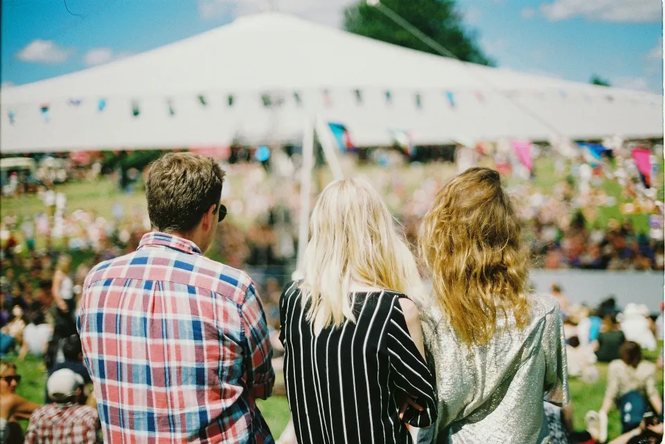 Three attendees watching an outdoor event from a grassy hill
